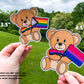A 3 1/2 inch and 4 1/2 inch sticker are shown held up next to each other for comparison. The 3 1/2 inch sticker has a progressive pride flag, the bow tie is rainbow with the center and dangles being the trans colors, brown, and black of the progressive part. The 4 1/2 inch sticker has a bisexual flag with a matching gradient bow tie. A note says all stickers are .666 inch not 1/2 inch but the number have been rounded for easier measurement.