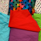The "New" fabric is in the upper left it has a white background with different breeds of dogs drawn in black and bones, paws, and tennis balls in the colors aqua, red, purple, and green the same shades as the 4 solid color fabrics below. The upper middle fabric is Black Rainbow Paws it has a blended rainbow background and medium sized black paw prints. The fabric on the upper right is called White Rainbow Paws it has a white background and small gradient rainbow paws.