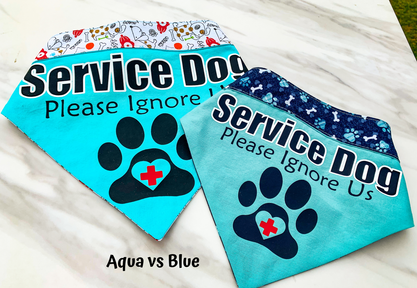 Aqua and Blue bandanas are shown for comparison. Aqua is much brighter and blue is a dulled blue color. Aqua has the old fire hydrant and bones contrast but this would be replaced with the new fabric. The blue fabric has the navy fabric with matching blue plaid paws, light blue hearts, and white bones for contrast. The blue fabric uses navy vinyl instead of black for aqua.