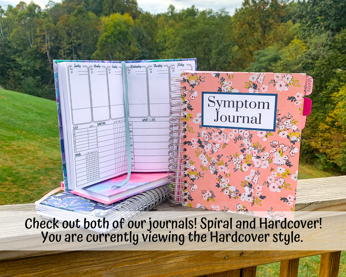One of the journals shown is sitting on top of another hardcover book in pink, and a blue spiral bound book. A large pink spiral bound book is shown closed to it's right with a label that says Symptom Journal. A note says check out both of our journals Spiral and Hardcover. You are currently viewing the hardcover style.