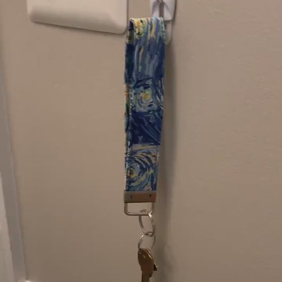  A video showing a starry night colored wristlet with keys attached is shown being taken off a hook on the wall and slipped on handed onto a wrist
