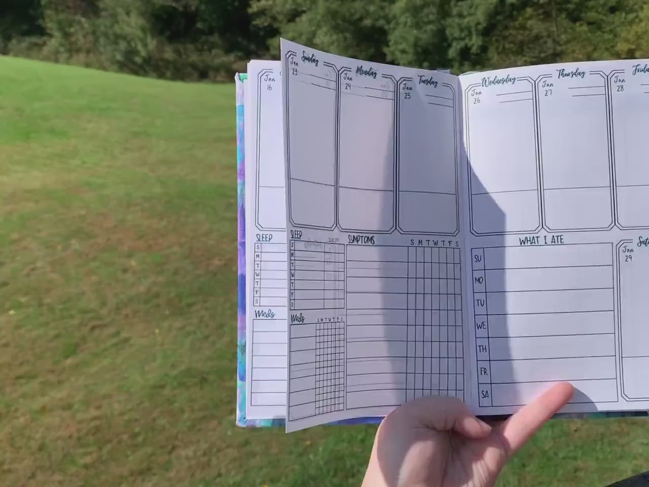 A video shows move left to right showing the main page of the symptom journal. The book is then opening laying down and is flicked to different pages to show what is in the book. The pages shown in order are the month page, main tracking page,then in the back medication and test history, doctor information, and lined pages