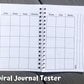 The spiral journal tester is shown open to the calendar page. There are 7 columns, 5 rows deep of squares with no dates. At the top of each column are the days of the week, but no color background. On the right page next to the box of squares you there are 3 vertical lines lining perpendicular to the way info would be written in the boxes. Notes is written on the left of the top line when facing to write. 