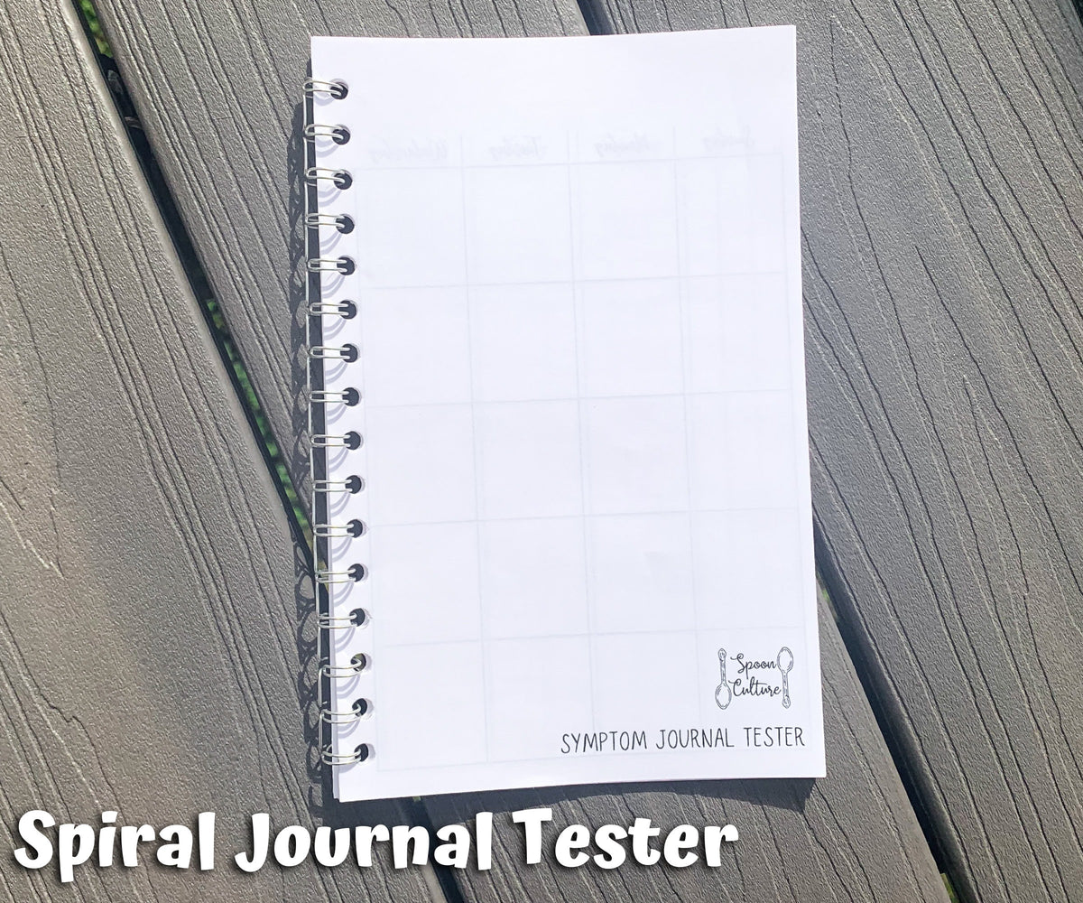 The spiral tester is shown on grey wood planks. It is closed and you can see the spoon culture logo on the front as well as the side of the coils. Text says spiral journal tester.