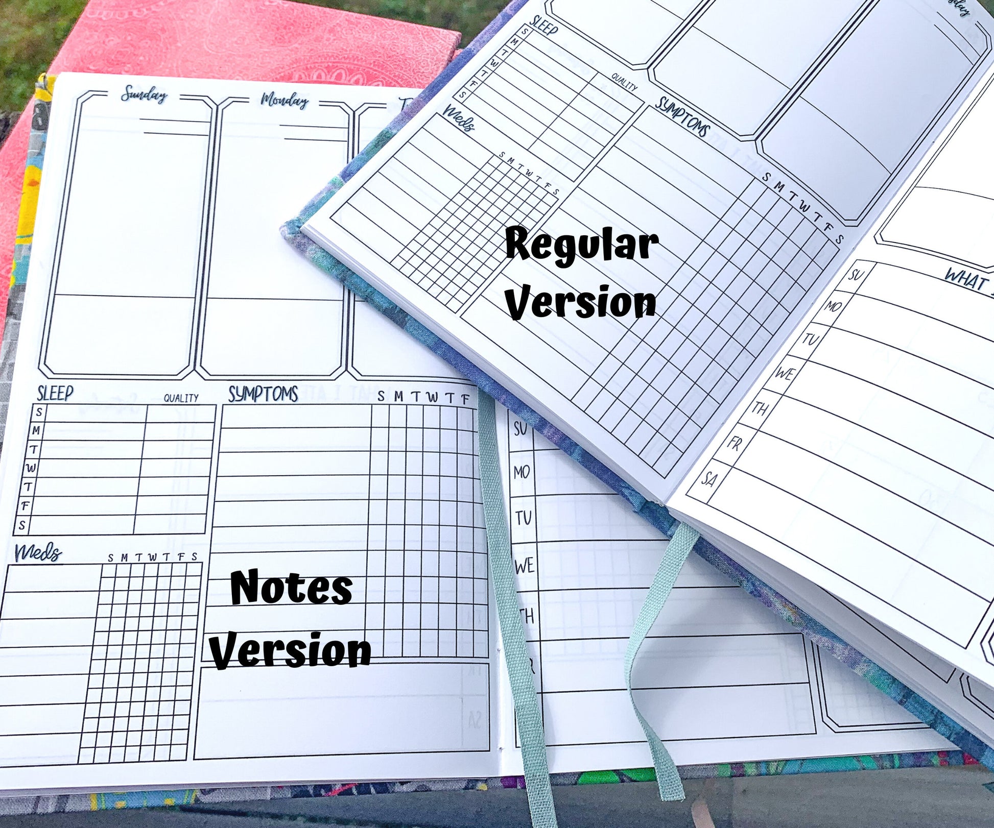 2 books are shown, open to the main tracking page. One book says Notes version and has a box below the symptom tracker, the symptom slots are shorter but they have the same amount. The other book says Regular version and does not have a box. You can see a piece of blue ribbon on both books that acts as a bookmark.