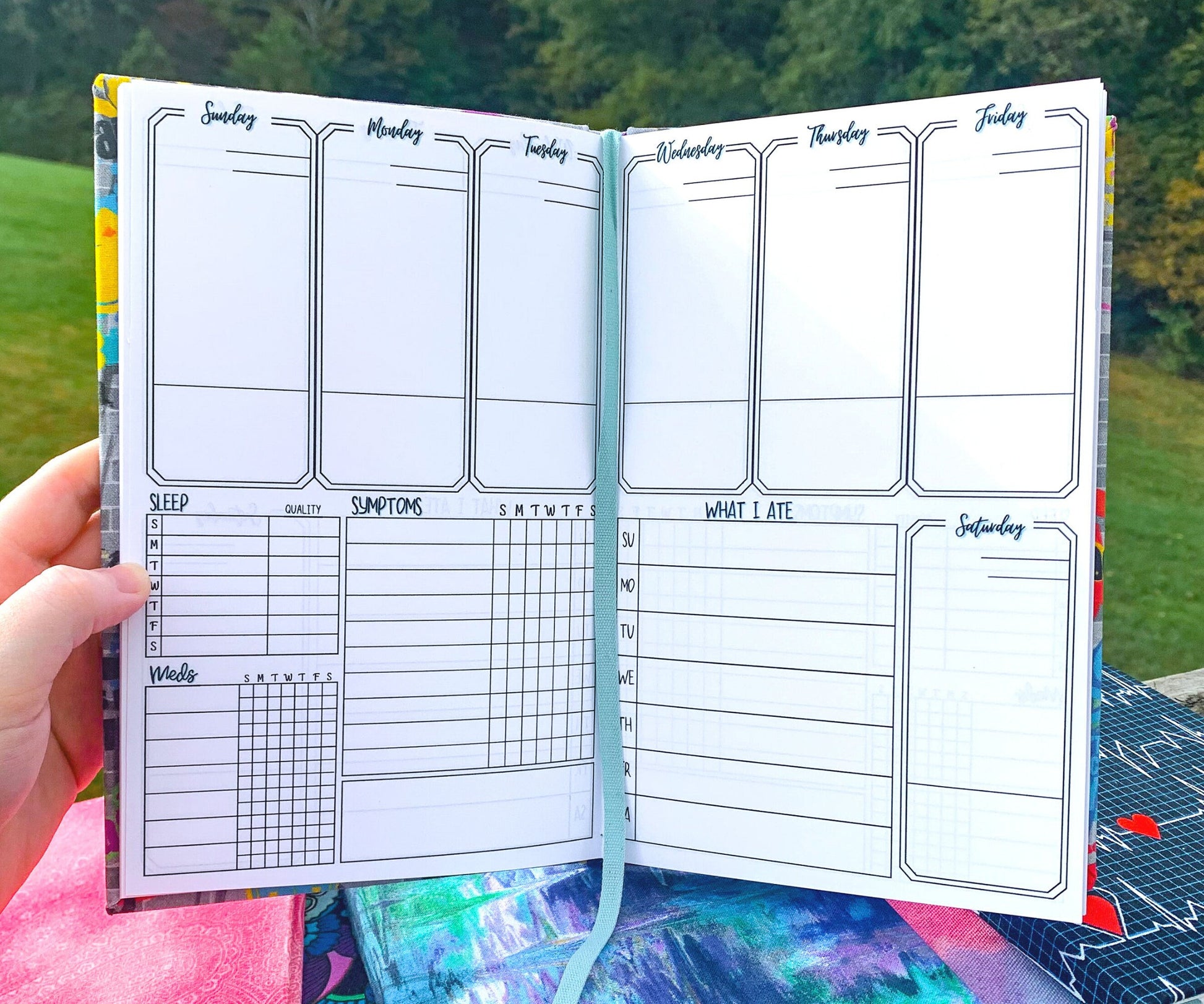 The week page of a symptom journal is shown. It has 6 boxes at the top and 1 below on the right, each is a day of the week. The boxes take up half the page vertically they have a line towards the bottom. Below on the left is a sleep, meds, and symptom tracker. Each has space for each day of the week. The med box has space 7 meds and 2 checkboxes per day. The symptom box has 10 slots. On the right is a what I ate box which is divided into writing slots for each day.