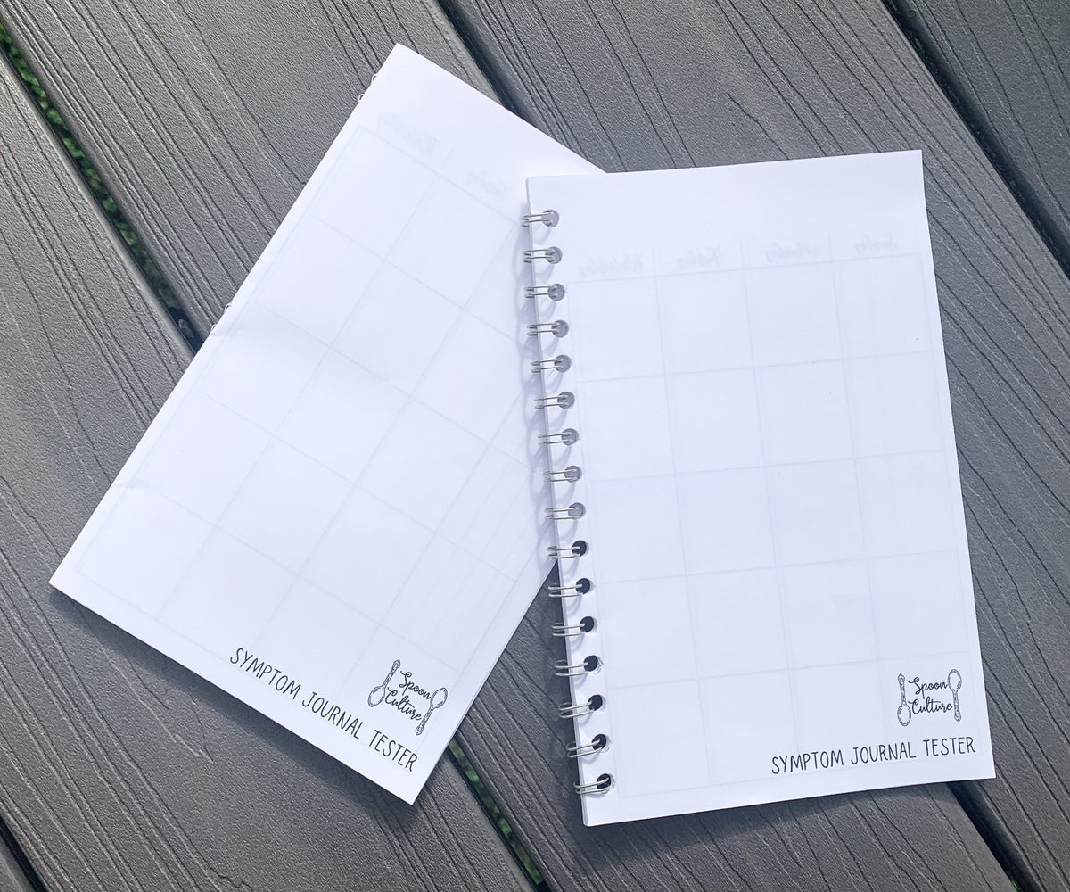 Both tester are closed on grey wood planks. Both have a logo in the bottom right corner that is two spoons in opposite directions with the words spoon culture in between, the words symptom journal tester are written below. The hardcover tester is on the left, it is flat folded pieces of paper. The spiral tester is on the right and you can see coils coming out of each hole punched.