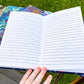 A book is open to lined pages, this is the back of the book. The book is sitting on top of multiple books with patterned covers.