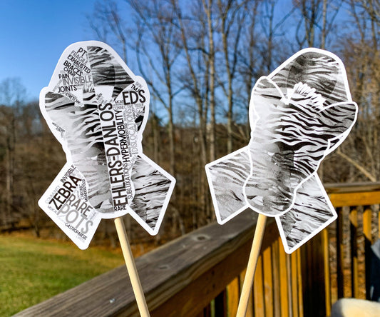 The word cloud and watercolor designs are shown on 2 sticks. Both ribbons are black and grey zebra stripes with a zebra head in the center. The word cloud design on the left is split in half with a word cloud on the left half of the ribbon and right half of the zebra. The right watercolor ribbon is all zebra patterened with a white border around the zebra for definition.