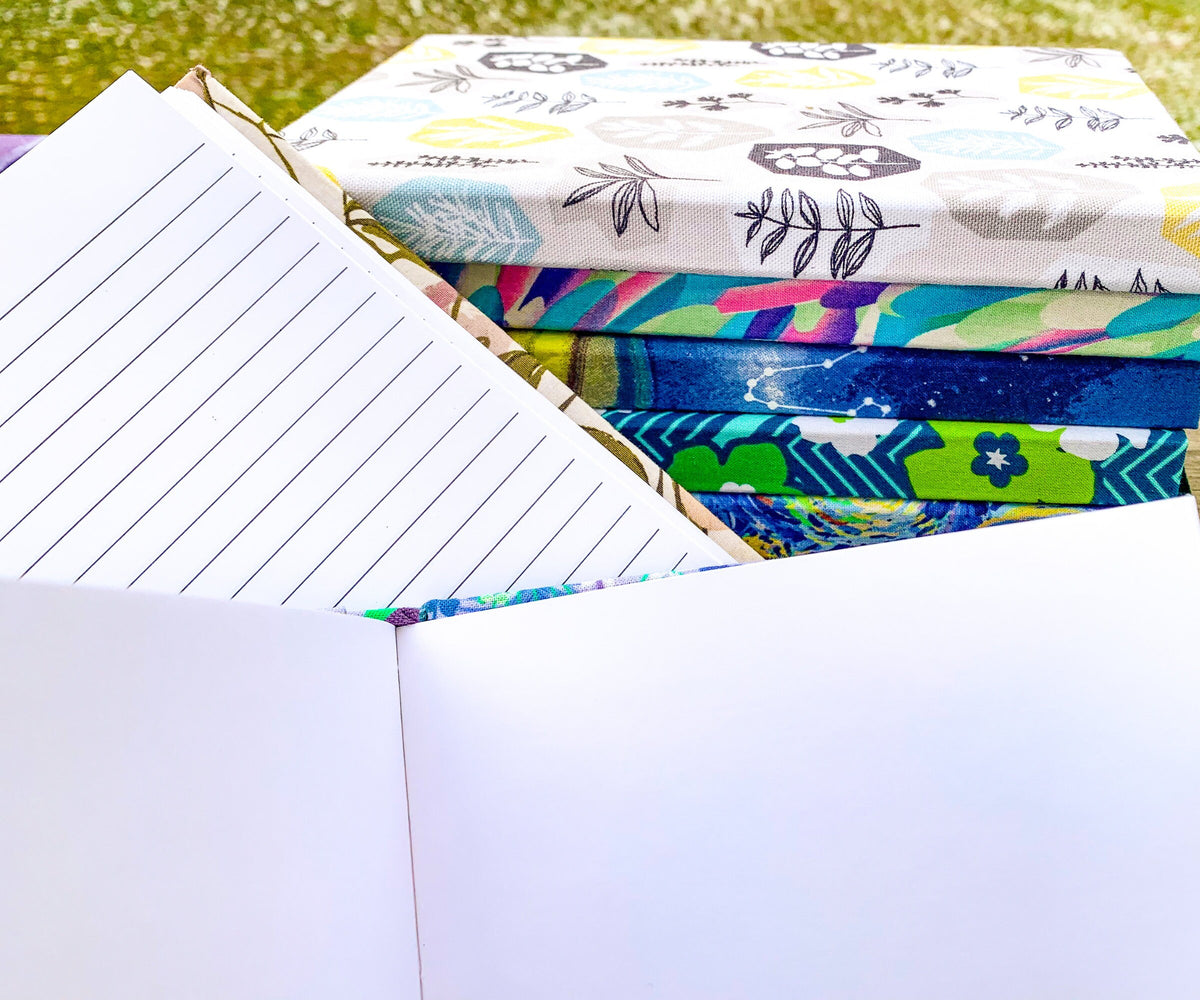 Open blank and lined books are shown next to a stack of books with patterned covers.