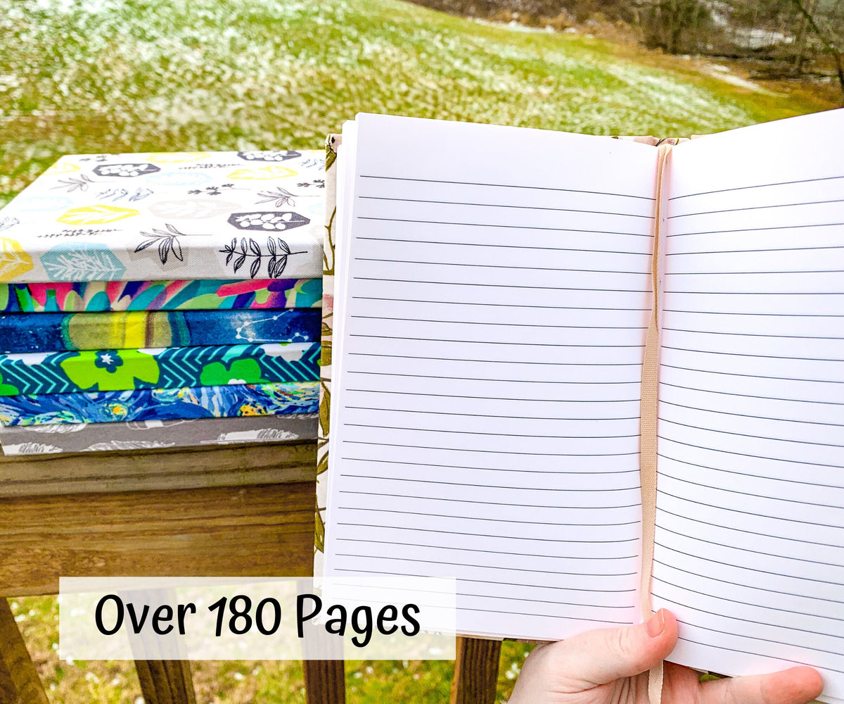 A lined book is shown open with a pink ribbon down the middle. A stack to the left has 6 books with various patterened covers. A note says over 180 pages.