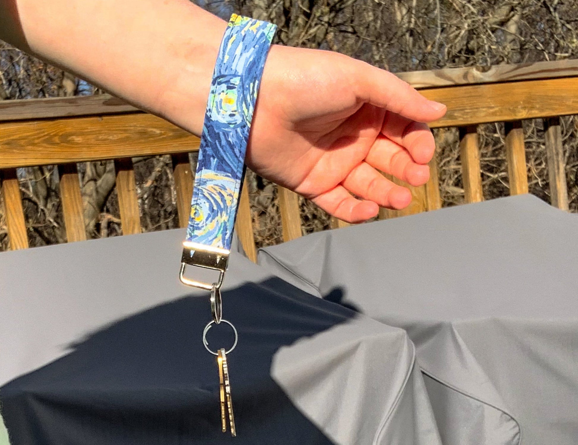 The starry night wristlet is shown hanging on a wrist. 2 Keys are attached the key loop. 